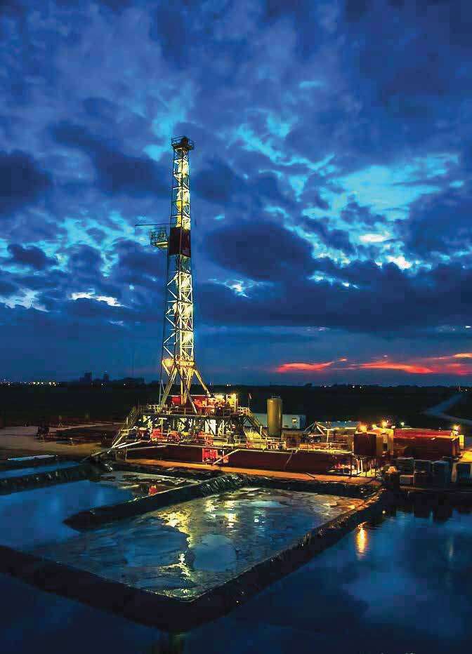 A drilling rig lit up against a dramatic blue dusk sky