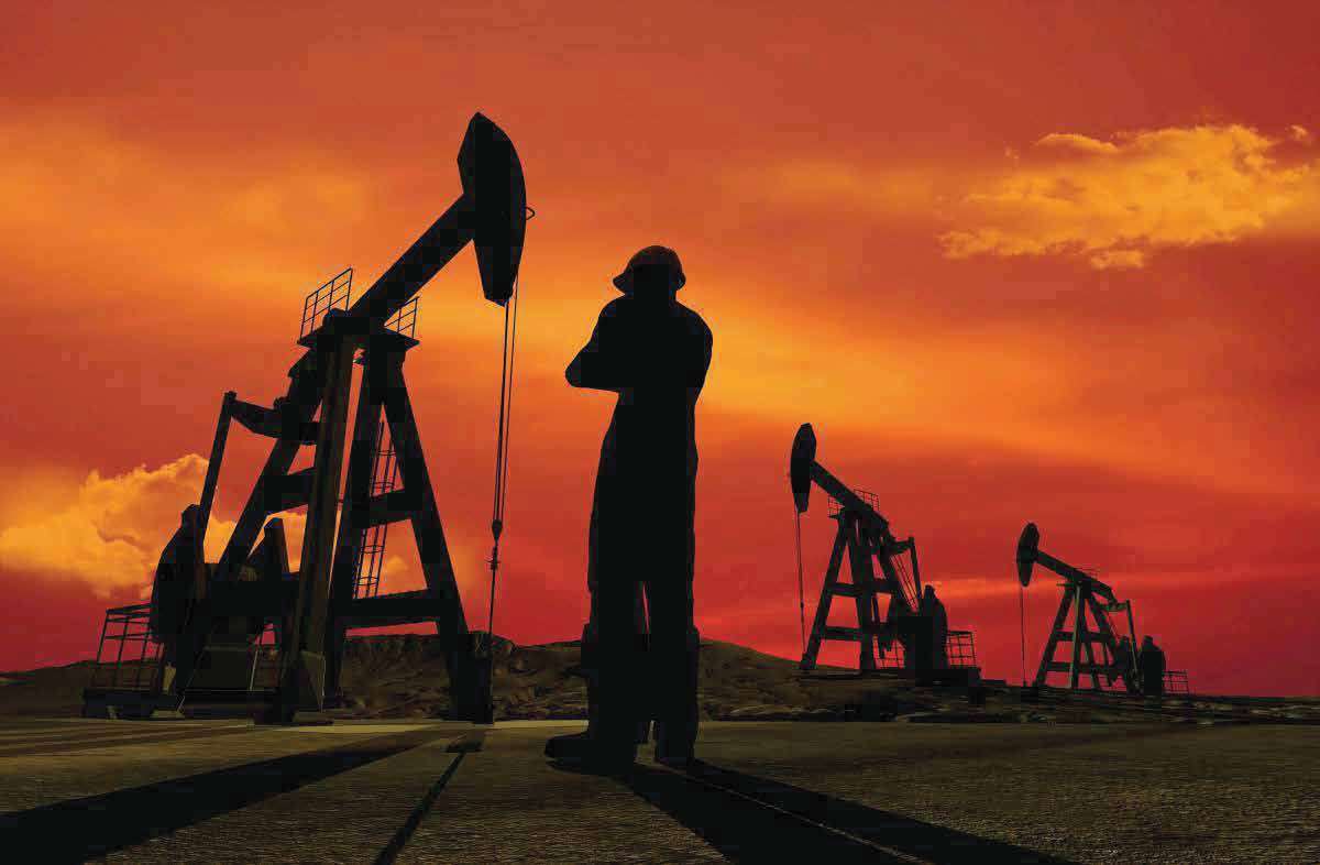A rig worker in silhouette watching over a row of pump jacks at sunset